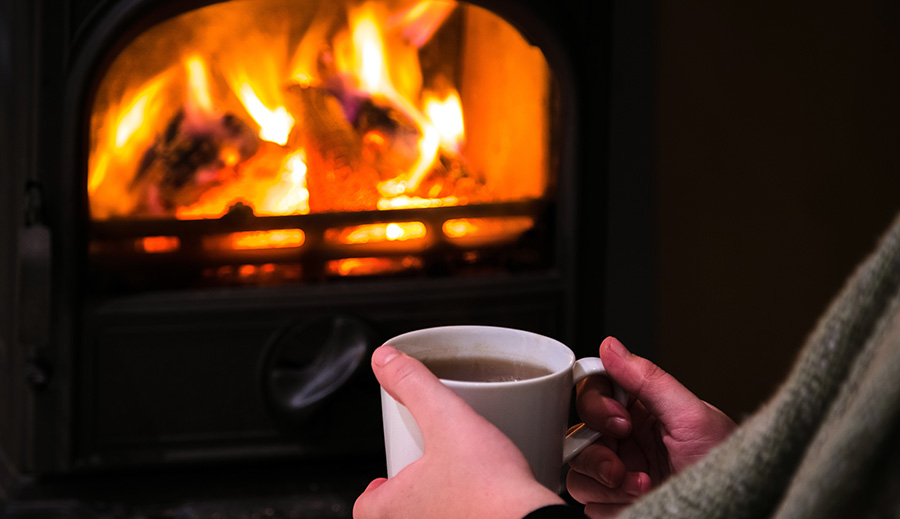 A woman enjoying a hot drink next to the fireplace